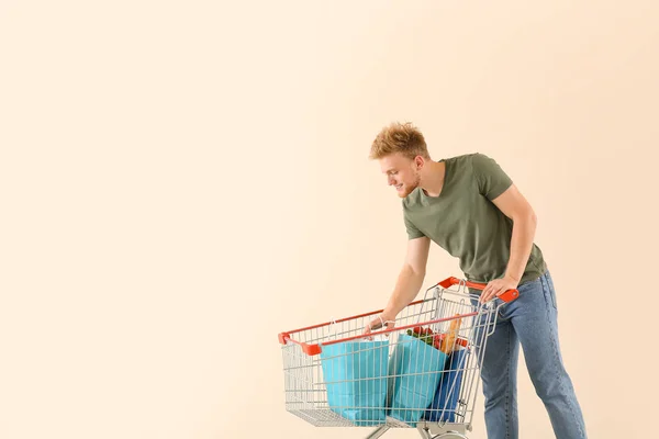 Young man with shopping cart on light background — Stock Photo, Image