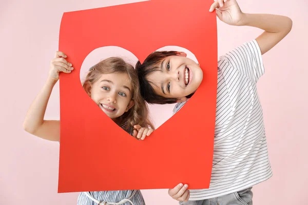 Söta små barn som håller pappersark med hål i form av hjärta på färg bakgrund. Alla hjärtans dag firande — Stockfoto