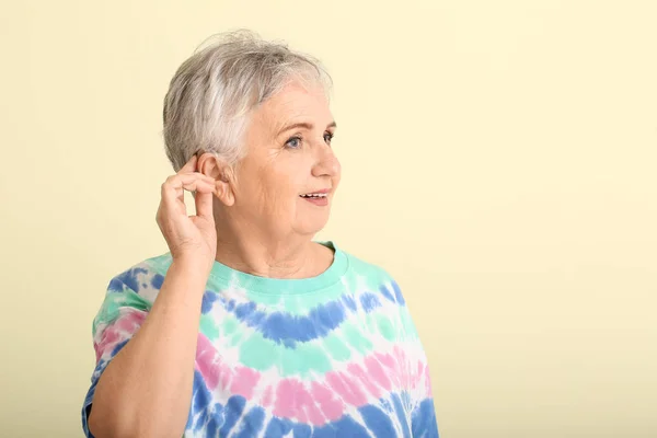 Senior woman with hearing aid on color background