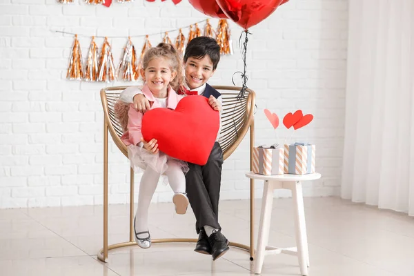 Schattige kleine kinderen met kussen in de vorm van een hart zittend in een fauteuil binnen. Valentijnsdag — Stockfoto