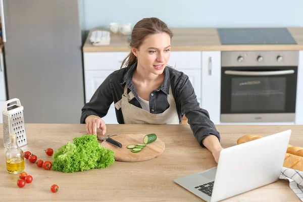 Mujer preparando sabrosa ensalada de verduras y el uso de ordenador portátil en la cocina —  Fotos de Stock