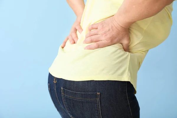 Mature woman suffering from back pain on color background — Stock Photo, Image