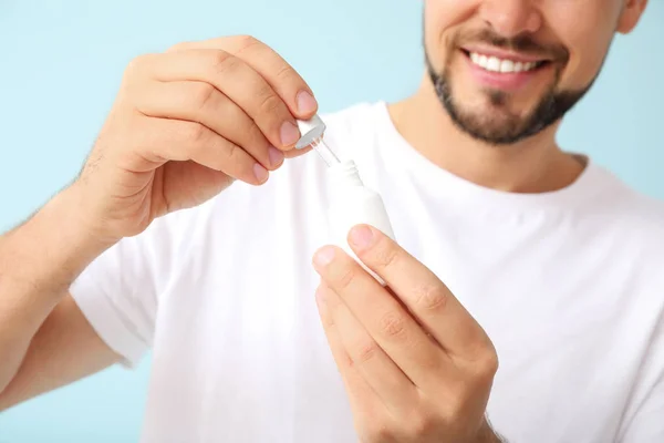 Homem bonito com produto cosmético sobre fundo de cor, close-up — Fotografia de Stock