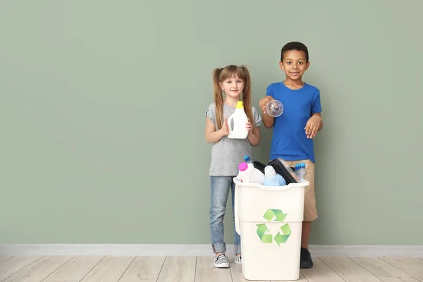 Niños pequeños y contenedor con basura cerca de la pared de color. Concepto de reciclaje — Foto de Stock