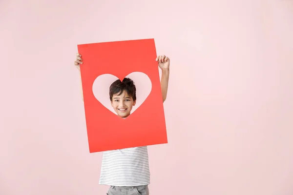 Ragazzino carino che tiene il foglio di carta con foro a forma di cuore sullo sfondo a colori. Festa di San Valentino — Foto Stock