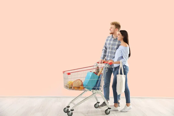 Renkli duvarın yanında alışveriş arabası olan genç bir çift. — Stok fotoğraf