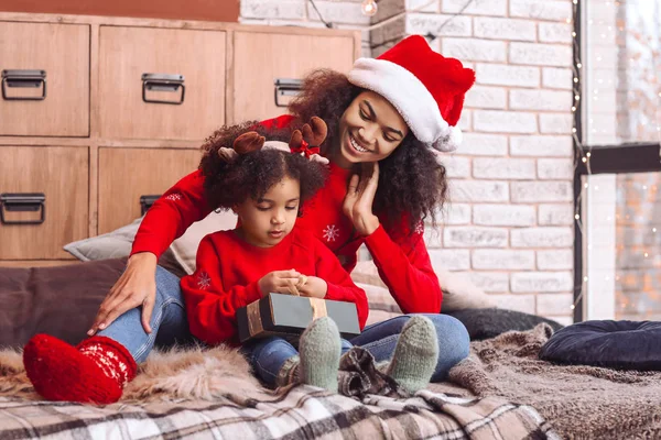 Happy African-American woman and her little daughter with gift at home on Christmas eve — Stock Photo, Image