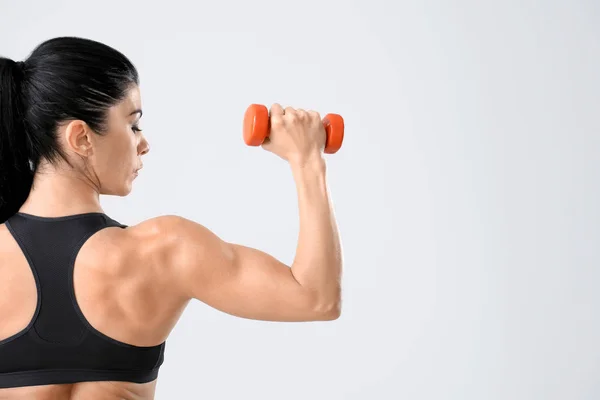 Mulher muscular desportiva com haltere no fundo claro — Fotografia de Stock