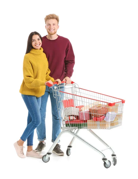 Young couple with shopping cart full of Christmas gifts on white background — Stock Photo, Image