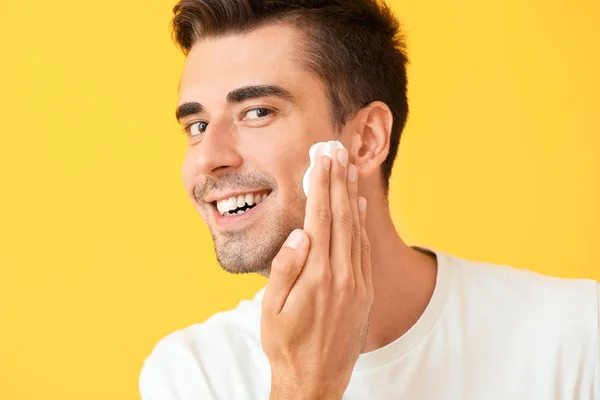 Schöner junger Mann, der Rasierschaum vor farbigem Hintergrund aufträgt — Stockfoto