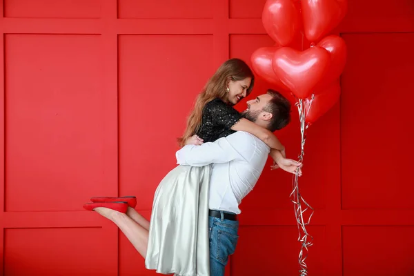 Jovem casal feliz com balões em forma de coração no fundo de cor. Celebração do Dia dos Namorados — Fotografia de Stock