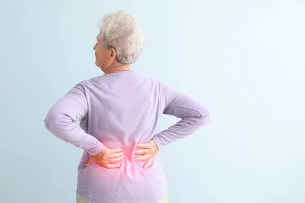 Senior woman suffering from pain in back against light background — Stock Photo, Image