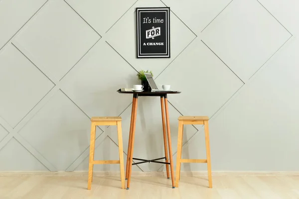 Stylish table with stools and laptop near grey wall in room — Stock Photo, Image