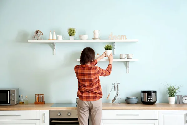 Mujer poniendo planta de interior en estante de la cocina —  Fotos de Stock