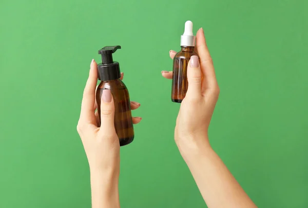 Farklı kozmetik ürünlere sahip kadın elleri renkli arka planda şişelerde — Stok fotoğraf