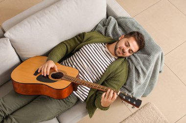 yakışıklı genç adam evde gitar çalıyor.