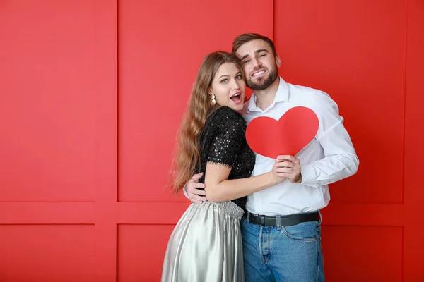 Glada unga par med rött hjärta på färg bakgrund. Alla hjärtans dag firande — Stockfoto