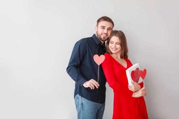 Glada unga par med hjärtan och gåva på ljus bakgrund. Alla hjärtans dag firande — Stockfoto