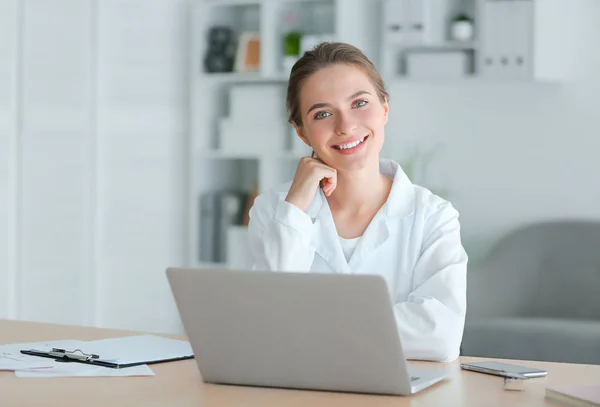 Kobieta lekarz z laptopem siedzi przy stole w klinice — Zdjęcie stockowe