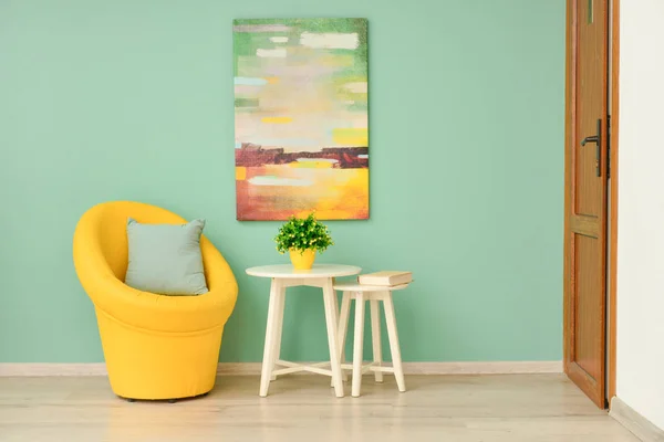 Poltrona elegante com mesas e planta perto da parede de cor no quarto — Fotografia de Stock