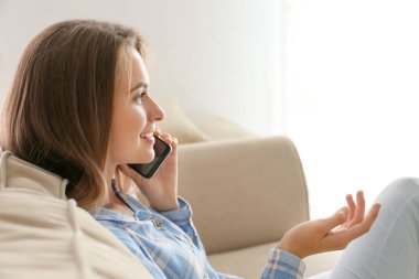 Evde cep telefonuyla konuşan genç bir kadın.