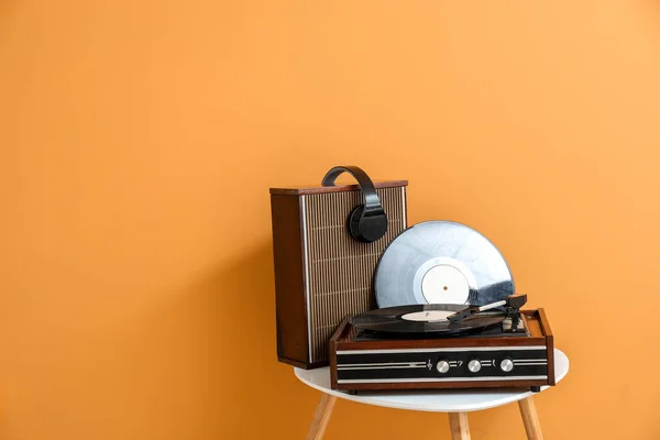 Grabar reproductor, altavoz, auriculares y disco de vinilo en la mesa cerca de la pared de color — Foto de Stock