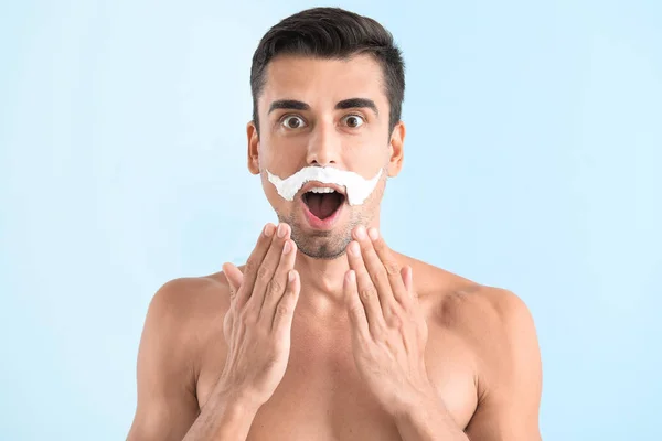 Surprised young man with shaving foam on his face against color background — Stock Photo, Image