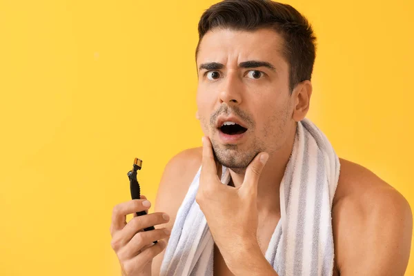 Displeased young man with razor on color background — Stock Photo, Image