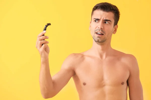 Displeased young man with razor on color background — Stock Photo, Image