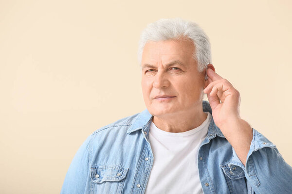 Зрелый мужчина со слуховым аппаратом на светлом фоне
