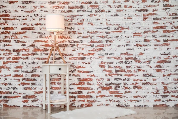 Стильний стіл зі світиться лампою біля цегляної стіни в кімнаті — стокове фото
