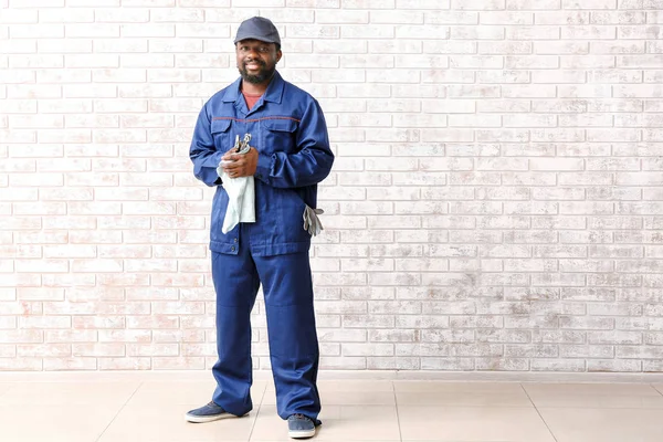 African-American car mechanic near brick wall