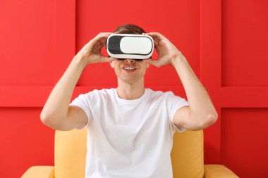 Sanal gerçeklik gözlüklü genç adam renkli arka planda koltukta oturuyor.