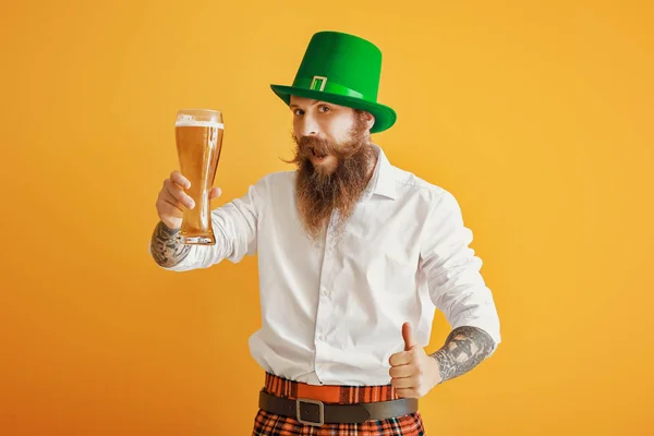 Homem barbudo com copo de cerveja mostrando gesto de polegar para cima no fundo de cor. Celebração do Dia de São Patrício — Fotografia de Stock