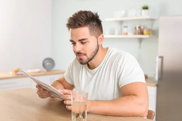 Handsome young man reading newspaper in kitchen — Stock Photo, Image