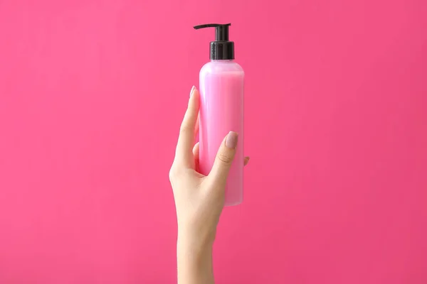 Mão feminina com produto cosmético em garrafa sobre fundo de cor — Fotografia de Stock