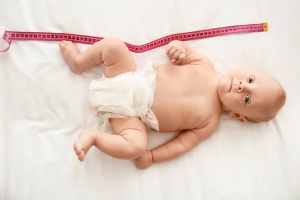 Cute little baby with measuring tape lying on bed, top view — Stock Photo, Image