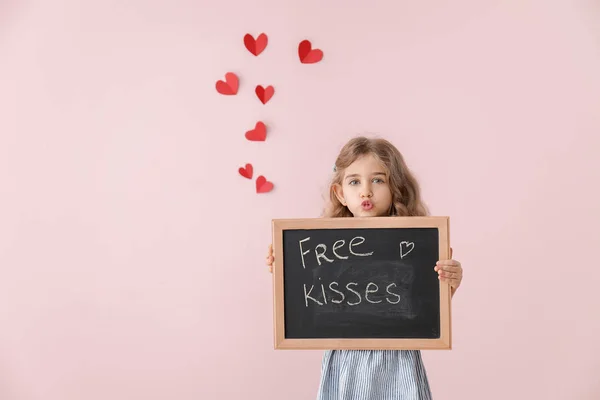 Carino bambina che tiene la lavagna con testo scritto baci gratuiti su sfondo a colori. Festa di San Valentino — Foto Stock