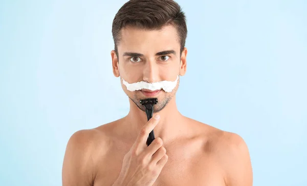 Handsome young man shaving on color background — Stock Photo, Image