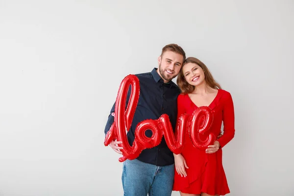 Jovem casal feliz com balão em forma de palavra AMOR no fundo de luz. Celebração do Dia dos Namorados — Fotografia de Stock