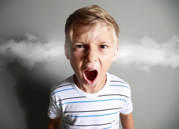 Retrato de niño enojado con vapor saliendo de las orejas sobre fondo gris — Foto de Stock