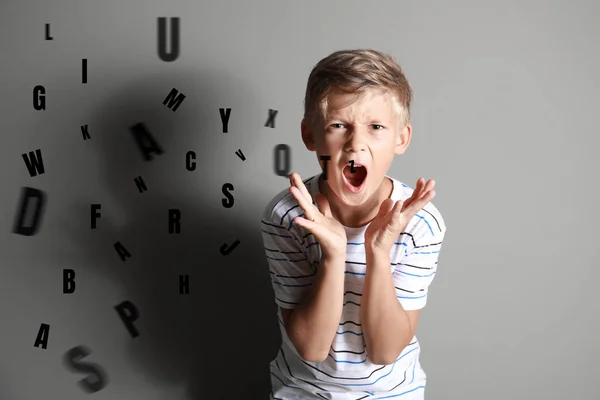 Porträt eines wütenden kleinen Jungen und Buchstaben des Alphabets auf grauem Hintergrund — Stockfoto