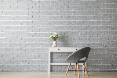 Vazodaki taze çiçekler masada ve tuğla duvarın yanındaki koltukta.