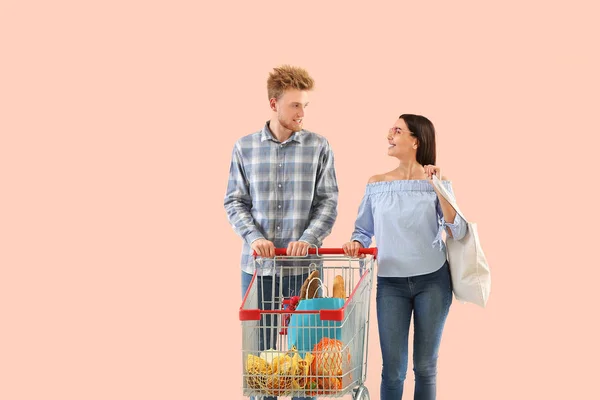 Young couple with shopping cart on color background — Stock Photo, Image