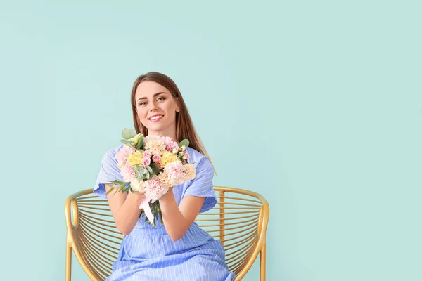 Vacker ung kvinna med bukett av nejlikor blommor sitter i fåtölj på färg bakgrund — Stockfoto