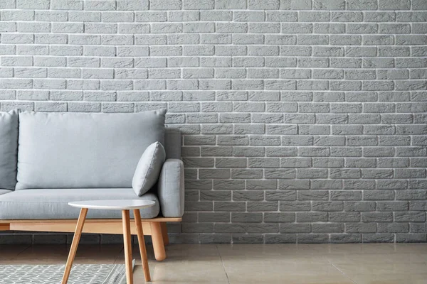 Yumuşak kanepe ve tuğla duvarın yanındaki masa — Stok fotoğraf