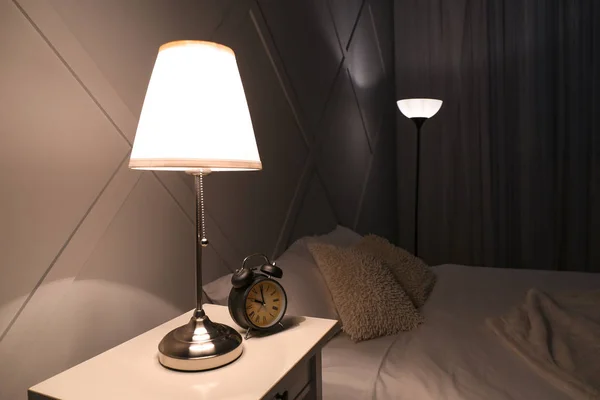 Lampa oświetlona z budzikiem na stole w sypialni — Zdjęcie stockowe