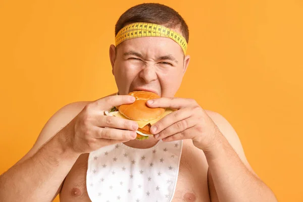 Uomo in sovrappeso con hamburger su sfondo colore — Foto Stock