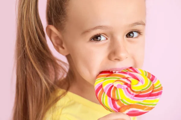 Cute little girl with sweet lollipop on color background — ストック写真