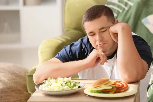 Избыточный вес мужчина выбор между здоровой и нездоровой пищи в домашних условиях — стоковое фото